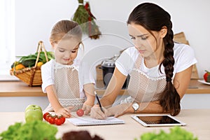 Happy family in the kitchen. Mother and child daughter make menue for cooking tasty breakfest in the kitchen. Little photo