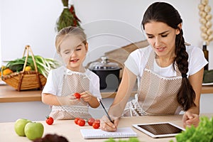 Happy family in the kitchen. Mother and child daughter make menue for cooking tasty breakfest in the kitchen. Little photo