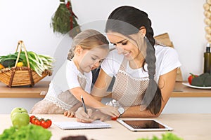 Happy family in the kitchen. Mother and child daughter make menue for cooking tasty breakfest in the kitchen. Little photo