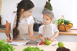 Happy family in the kitchen. Mother and child daughter make menue for cooking tasty breakfest in the kitchen. Little photo