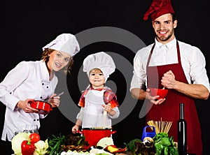 Happy family in kitchen preparing healthy food. Adorable son in chef hat with parents cooking together homemade food