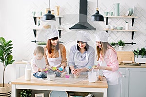 Happy family in the kitchen. Young woman and her sister, middle aged woman and little cute daughter cooking cupcakes for