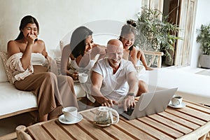 Happy Family With Laptop Having Fun Together. Dad, Mom And Daughters Sitting On Sofa In Patio.