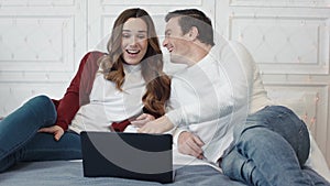 Happy family laughing in front of laptop screen in living room.