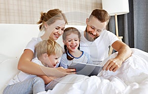 Happy family laughing with tablet computer in bed at home. watching movies and   Internet