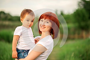 Happy family leisure outdoors. Portrait of smiling young woman holding little toddler son in arms, green background