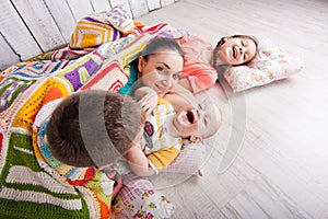 Happy family lie on the floor under colorful blanket and laugh.