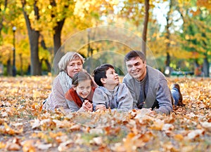 Happy family lies in autumn city park on fallen leaves. Children and parents posing, smiling, playing and having fun. Bright yello