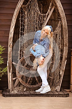 Happy family lifestyle concept. Family look. Portrait of Blonde Mother playing her daughter hugging by boat with fishing net.