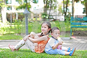 Happy Family. Little Asian sister and her younger brother sit back and lean back together in the green garden. Child girl cuddle
