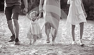 A happy family with little baby girl goes and holds hands while walking