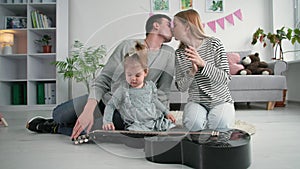 happy family, little beautiful girl playing with musical instruments in background mom claps hands and dad kisses his