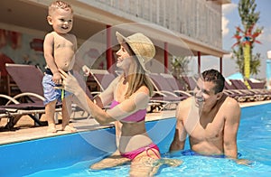 Happy family with little child resting in swimming pool