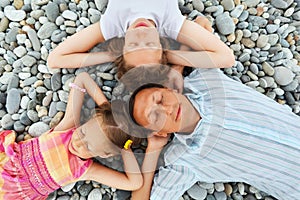 Happy family with little girl lying on stony beach