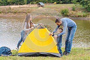 Happy family with little son set up camping tent. Happy childhood, camping trip with parents. A child helps to set up a tent