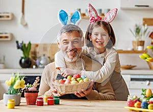 Happy family loving grandfather and cute little girl granddaughter embracing while painting Easter eggs