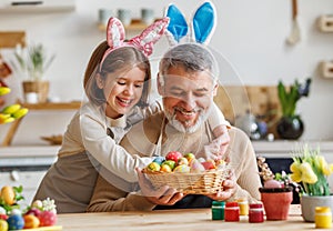 Happy family loving grandfather and cute little girl granddaughter embracing while painting Easter eggs