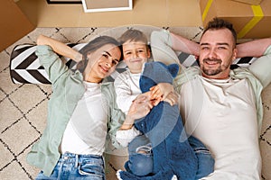 Happy family lying on the floor in new home with cordboard boxes around