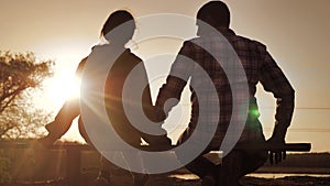 Happy family man and girl teamwork sitting on a bench silhouette sunset in lifestyle the park and nature. dad and