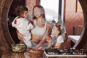 Happy family members. Young mother with kids standing in the kitchen and have some fun