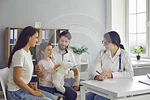 Happy family in modern pediatrician`s office consulting friendly young female doctor