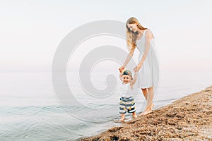 Happy family, mom and baby are walking along the evening beach during sunset