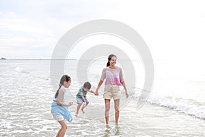 Happy family mom and child having fun in summer holiday. Asian mother and kids enjoy playing on tropical sand beach at sunrise