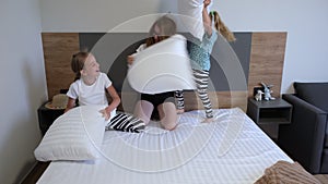 Happy family of mom and cute children siblings girls playing pillow fight on bed. Cheerful mother laughing having fun