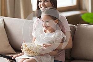 Happy family mom with cute kid daughter watching tv together