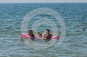 Happy family mom, dad and daughter play on an air mattress swimming in the sea photo