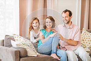 Happy family, mom dad and daughter are sitting on couch and laughing together