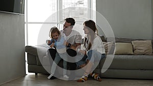 Happy family mom and dad having fun with little girl on cozy home grey sofa. Little daughter having fun with young