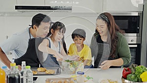 Happy family mom dad and kids siblings cooking together, parents teaching children son daughter cooking fresh vegetable salad and