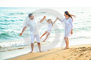 Happy family mom, dad and little daughter walk along the coast on sea beach at resort