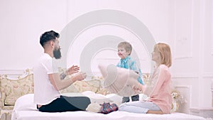 Happy family mom, dad and little son having fun pillow fight on bed, young mother, father child boy laughing feel joy