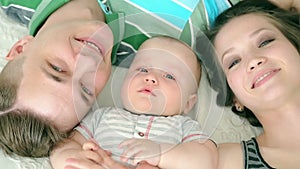 Happy family. Mom dad and six month old baby. Family lying in bed and looking at the camera, smiling.