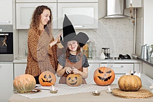 Happy family: mom and daughter celebrate Halloween. Merry child in witch carnival costume in the room. Cheerful kid and