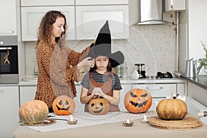 Happy family: mom and daughter celebrate Halloween. Merry child in witch hat at home kitchen. Cheerful kid and parent