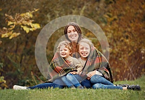 Happy family mom, daughter and little son sitting on the grass and they all laugh sunny autumn day