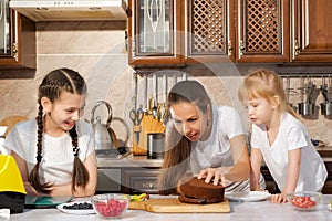 Happy family mom and daughters are cooking birthday cake together.