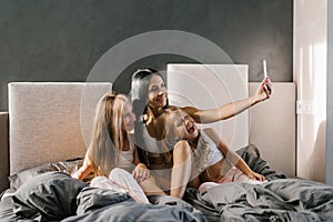 Happy family mom and daughters in pajamas in the morning in bed taking selfies on a smartphone or video chat