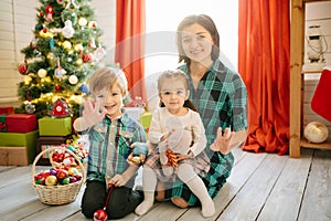 Happy family mom, son and daughter on a Christmas winter sunny morning in a decorated Christmas celebration room with a