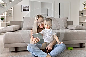 Happy family mom teaching cute child son using digital tablet at home.