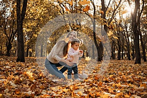 Happy family mom and toddler baby girl playing outdoors in fall park. Little girl and her mother in the autumn park