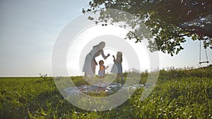 Happy family of mom and two little daughters are resting in a meadow, far from the city.