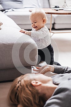 Happy family moments. Mother lying comfortably on children& x27;s mat playing with her baby boy watching and suppervising