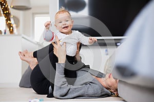 Happy family moments. Mother lying comfortably on children& x27;s mat playing with her baby boy watching and suppervising