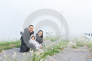 happy family in morning with cold weather and fog covering area, father mother take their cute little daughter come see fog feel