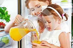 Happy family mother and baby daughter drinking orange juice in