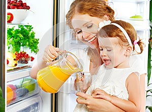 Happy family mother and baby daughter drinking orange juice in